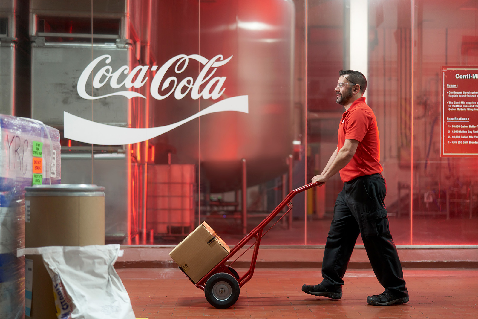Man pushing dolly cart with cardboard box at Coca-Cola factory